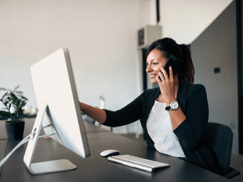 vrouw met gsm in de hand aan het bellen, wijst naar computerscherm