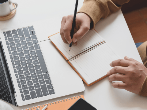 man aan laptop heeft een potlood vast en noteert in notitieblok